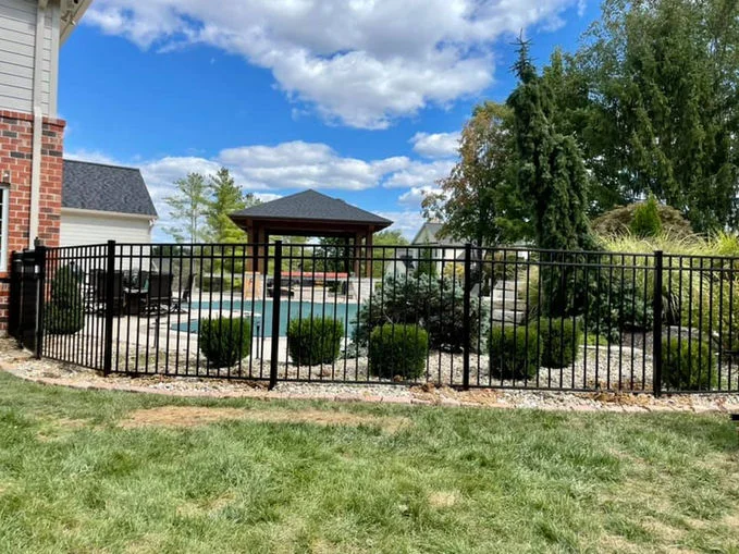Black aluminum fence near bushes and a house