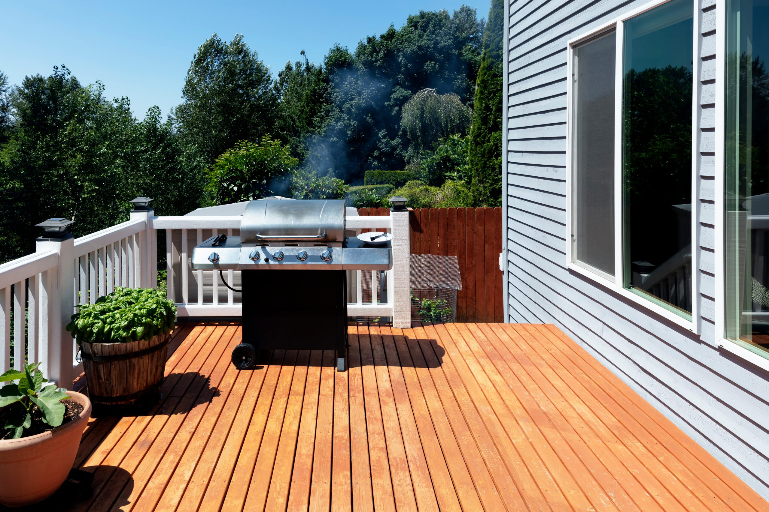 Large outdoor BBQ cooker with smoke coming out while on home wooden deck